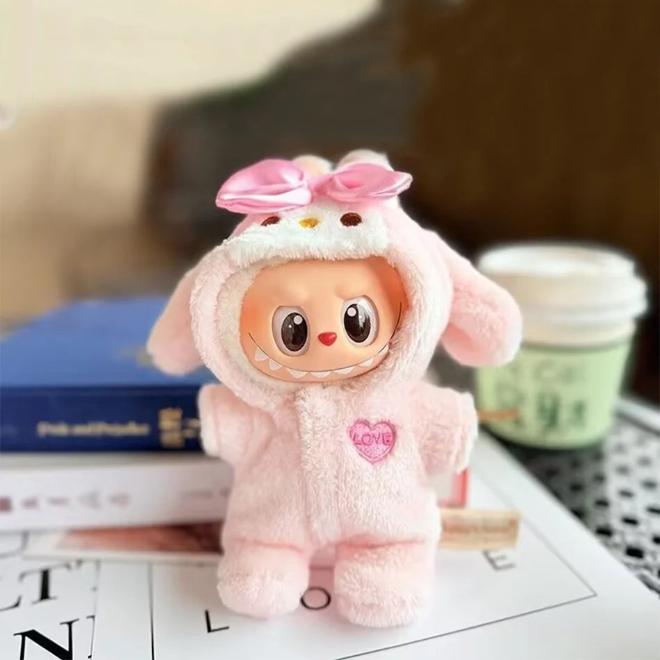 A Labubu figure wearing a fluffy pink bunny bodysuit with a large pink satin bow on the head and a pink heart emblem on the chest. The figure is standing on a book in front of a coffee cup.