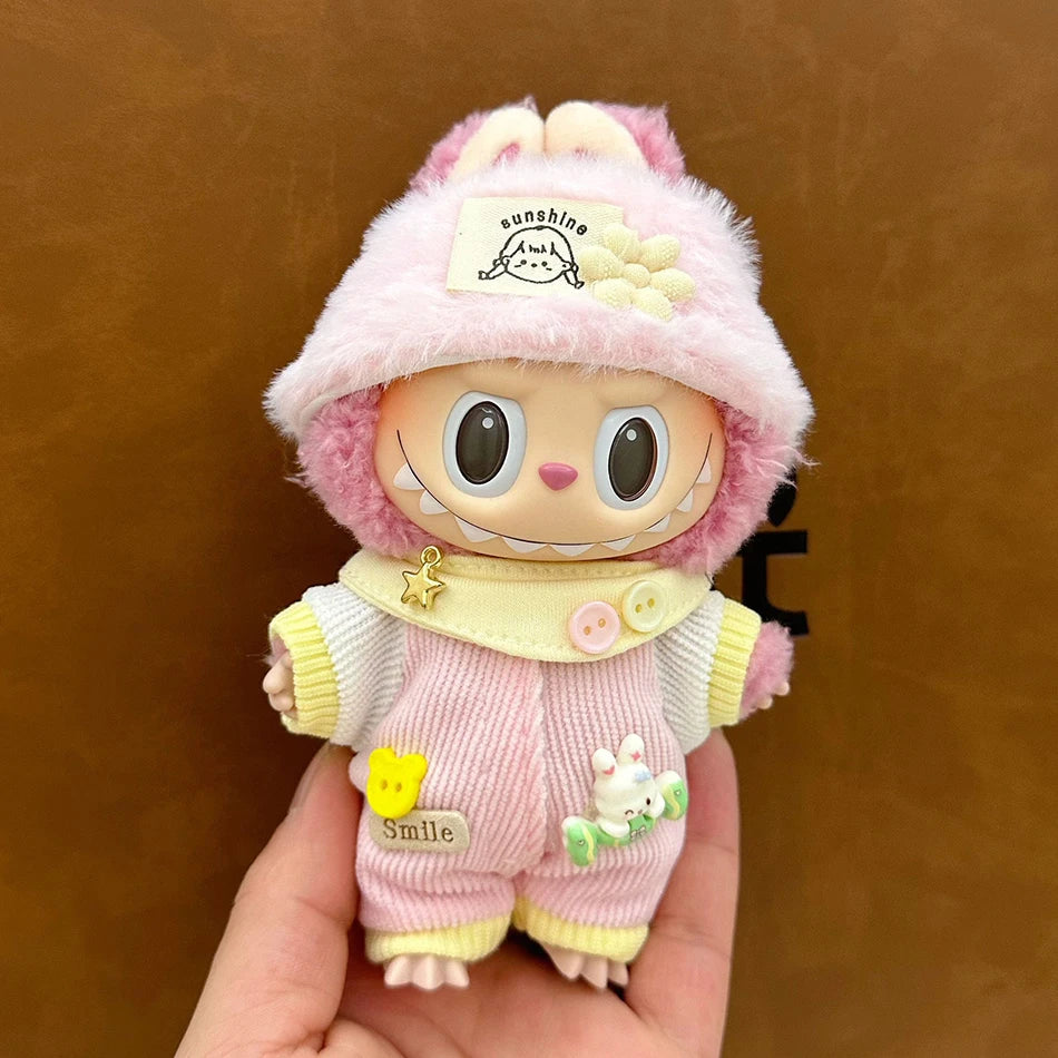 Labubu wearing a cozy pastel outfit with a pink corduroy jumpsuit, striped shirt, and fluffy hat with a flower.