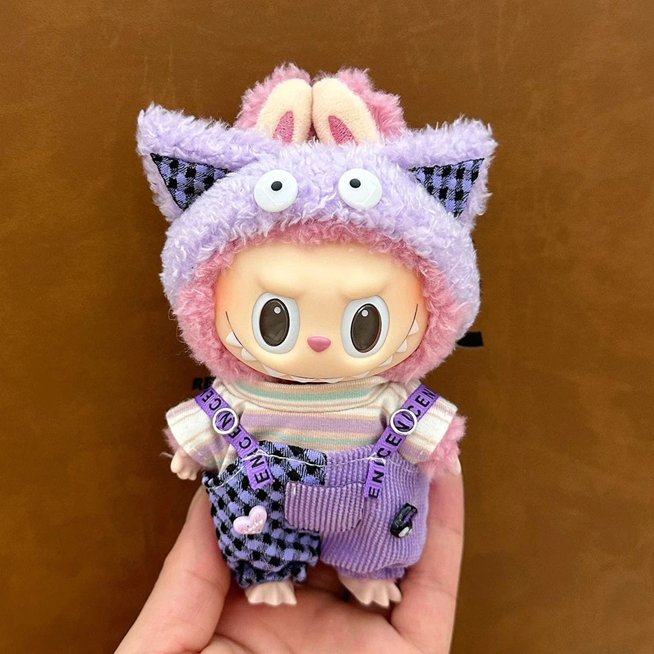 Labubu wearing a lavender plaid outfit with corduroy overalls, a striped shirt, and a plush hoodie with googly eyes.
