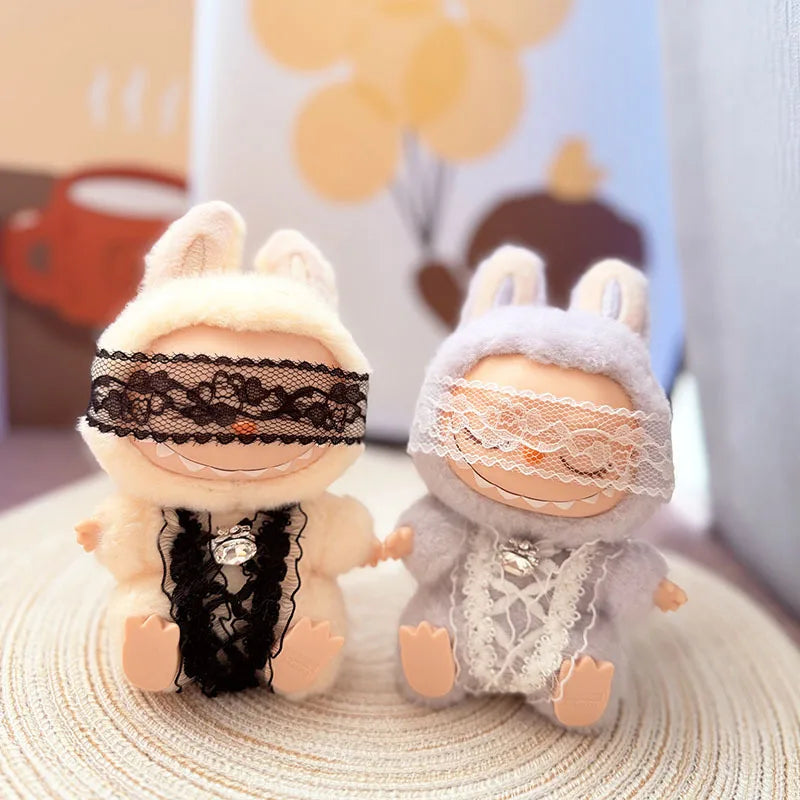 Two Labubu figures in matching cozy lace dreamer outfits, one in white and one in lilac, with blindfolds and crystal charms.