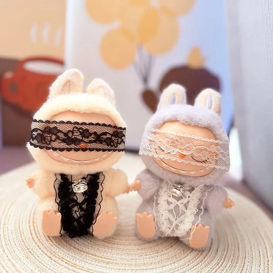 Two Labubu figures in matching cozy lace dreamer outfits, one in white and one in lilac, with blindfolds and crystal charms.